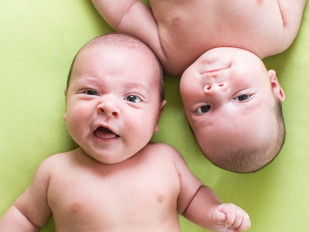 newborn twin babies making faces while lying on a green surface