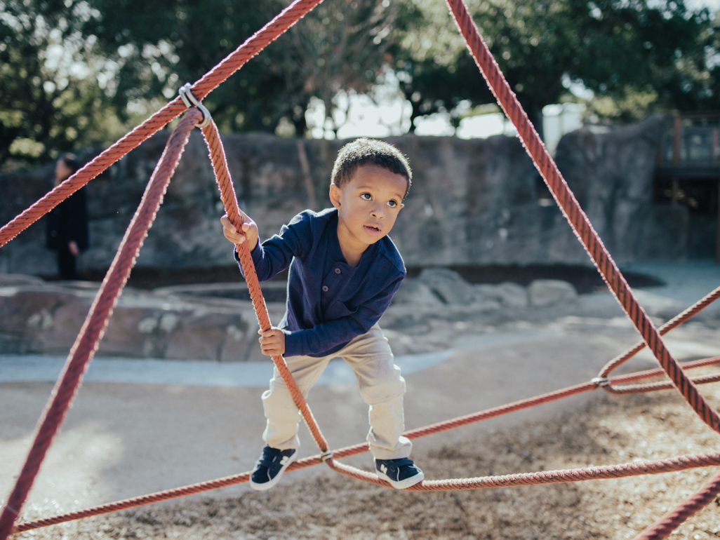 young boy climbing on rope structure at playground