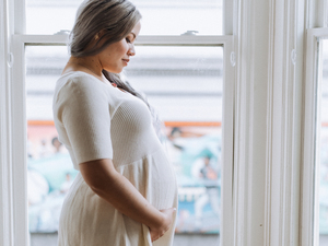 side profile view of a pregnant woman showing off her belly bump in front of a window