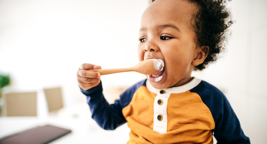 young boy spoon feeding himself yogurt
