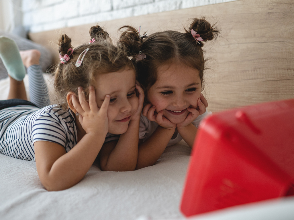 twin girls on bed looking at tablet