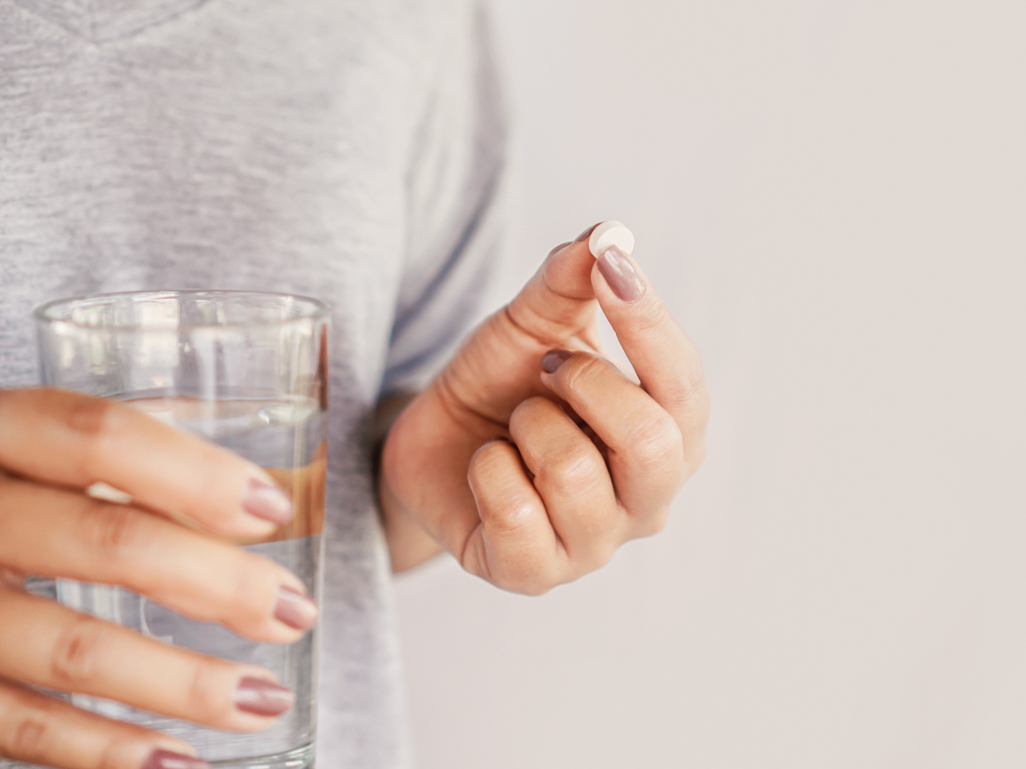 close up of woman holding a pill and glass of water