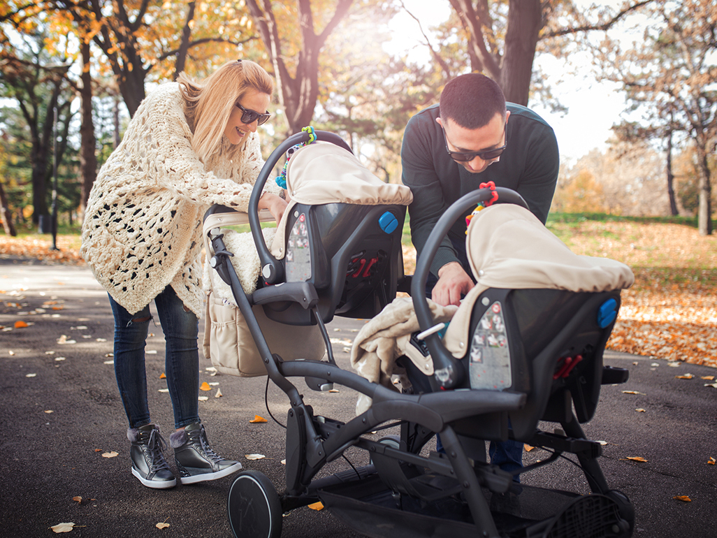 couple with double stroller taking care of each child separately at the same time while staying at the park