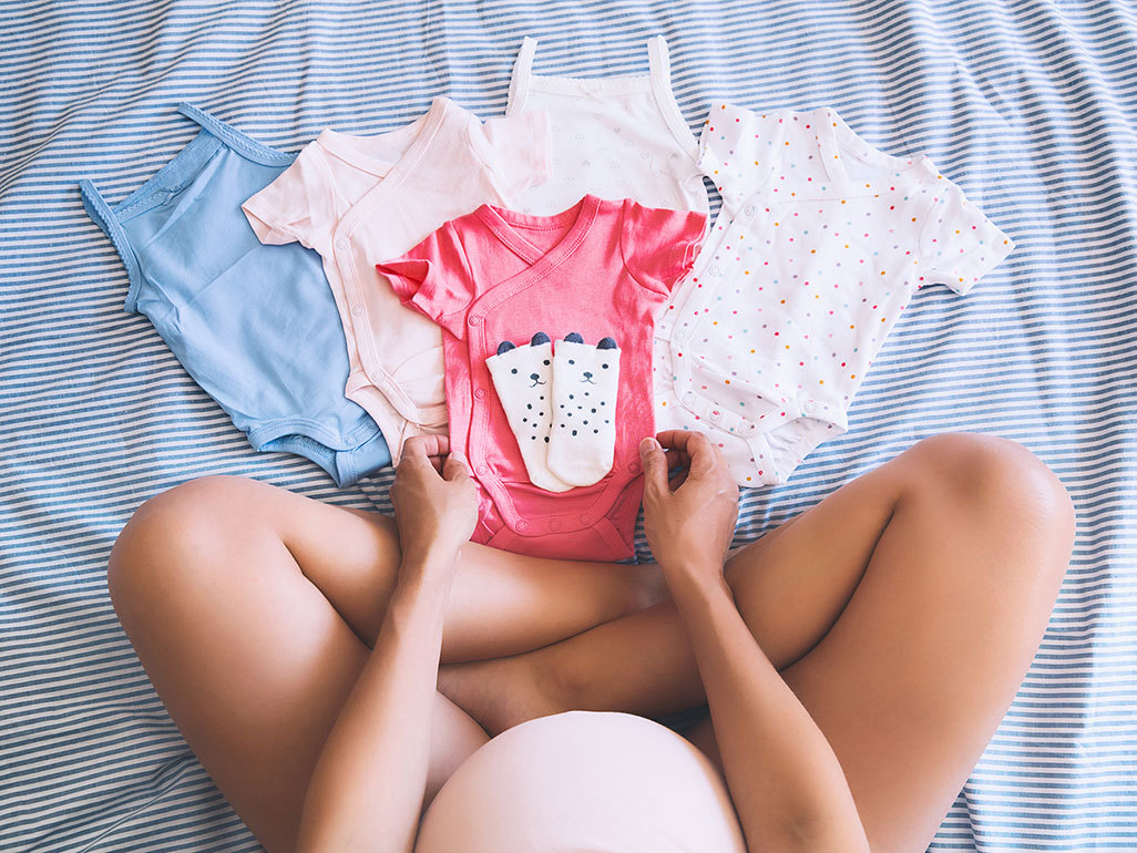 pregnant woman looking down at baby onesies