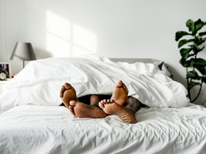 Two people lay under a blanket in bed, with their feet hanging out of the blanket