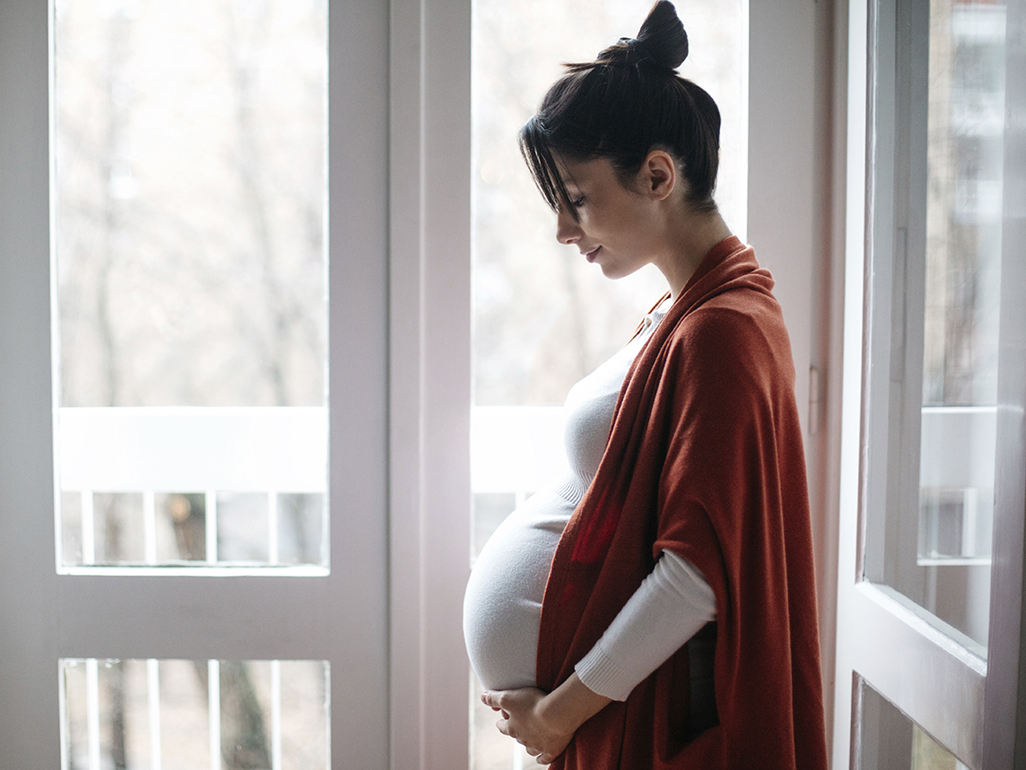 side view of a pregnant woman looking down at her pregnant stomach