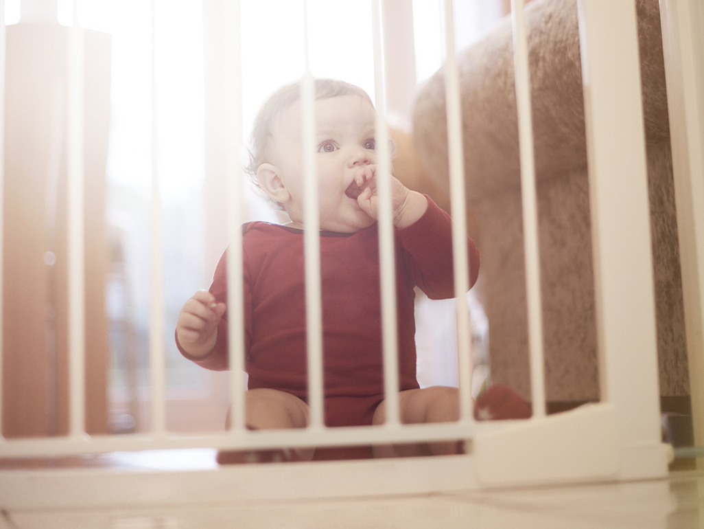 baby with fingers in mouth sitting on a floor behind the baby fence